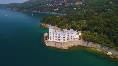 Through-the-lens-of-a-drone-camera,-one-can-appreciate-the-majestic-beauty-of-Miramare-Castle,-elegantly-perched-by-the-sea