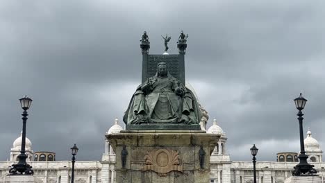 Low-angle-shot-of-statue-of-Queen-Victoria-sitting-in-front-of-Victoria-Memorial-in-Kolkata,-India-with-dark-clouds-passing-by