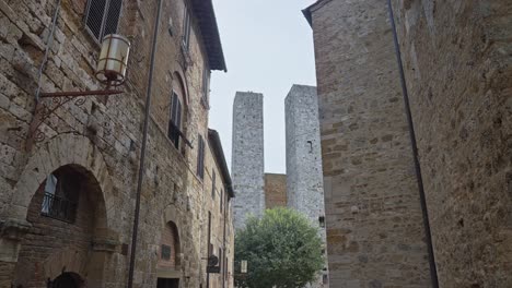 Gente-Caminando-Por-Las-Calles-De-La-Ciudad-Medieval-Con-Torri-Dei-Salvucci-Al-Fondo-En-San-Gimignano,-Italia.