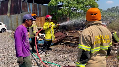 Indonesian-firefighter-holding-a-hose-and-extinguish-fire,-slow-motion,-handheld