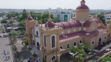 Aerial-orbiting-shot-of-cathedral-de-San-Cristobal-with-flying-pigeons-during-sunny-day,-Dominican-Republic