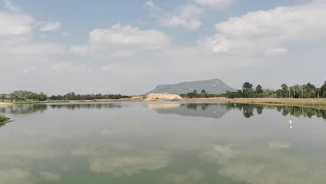Wunderschöner-Malerischer-See-Mit-Einer-Klaren-Spiegelreflexion-Eines-Hinüberfliegenden-Vogels-In-Phetchaburi,-Thailand
