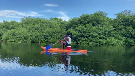Local-black-strong-man-rowing-in-kayak-in-mangroves-lake-at-day-time