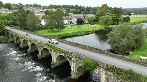 Kilkenny-Ireland-Inistioge-aerial-static-of-the-river-and-bridge-with-the-village-park-on-a-summer-morning-with-a-cycle-race-crossing-the-bridge