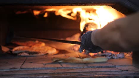 Der-Chefkoch-Verwendet-Einen-Langen-Pizzaschieber,-Um-Pizzen-In-Den-Traditionellen-Holzofen-Zu-Bewegen
