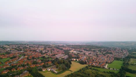 Drone-footage-showcases-the-fame-of-Dewsbury-Moore-Council-estate,-a-renowned-UK-urban-housing-complex,-red-brick-terraced-homes,-and-the-industrial-Yorkshire-landscape-on-a-summer-evening