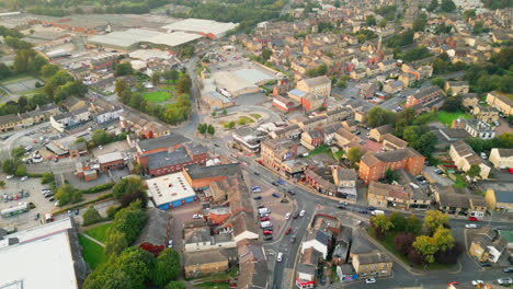 A-drone-records-Heckmondwike,-UK,-with-industrial-buildings,-bustling-streets,-and-the-old-town-center-on-a-summer-evening