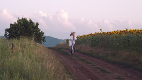 Girl-in-white-dress-rides-bike-in-rural-countryside-at-golden-hour-slow-mo