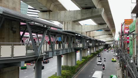 Busy-Road-Below-with-BTS-Skytrain-Walkway-and-People-Walking-in-Bangkok,-Thailand