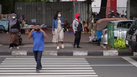 Un-Hombre-Que-Llevaba-Una-Máscara-Mientras-Cruzaba-La-Calle-Frente-A-Los-Agentes-En-La-Estación-Senen,-Yakarta.