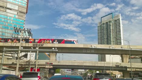BTS-Skytrain-Crosses-Over-an-Intersection-While-Vehicles-Wait-in-Traffic-on-a-Clear-Blue-Sky-Day-in-Bangkok,-Thailand