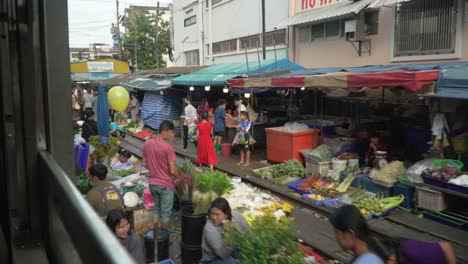 Pov-from-train-window-showing-street-market-in-Bangkok-city-near-rails,-slow-motion