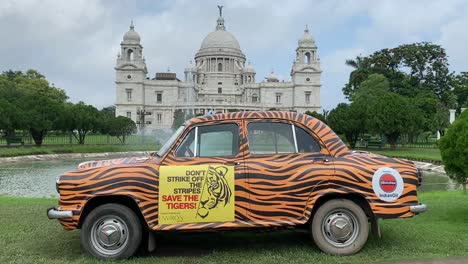 Beautiful-shot-of-yellow-taxi-advertising-tiger-conservation-program-with-view-of-Victoria-Memorial-in-the-background-in-Kolkata,-India-on-a-cloudy-day