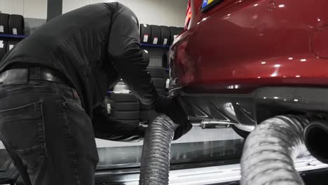 Mechanic-fitting-garage-exhaust-removal-system-to-prevent-dangerous-exhaust-from-passenger-vehicle