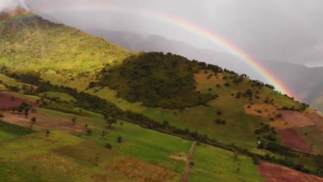 Aerial-View-of-Beautiful-Multicolor-Rainbow-in-the-Sky-Above-Mountains-and-Green-Fields-in-Ecuador
