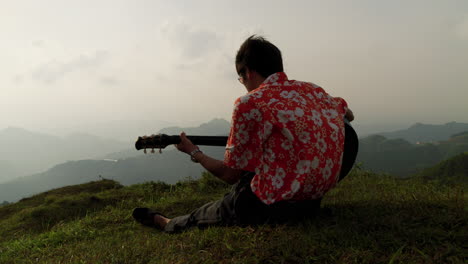 Male-playing-guitar-on-hill-top-in-beautiful-nature-enjoying-evening-breeze