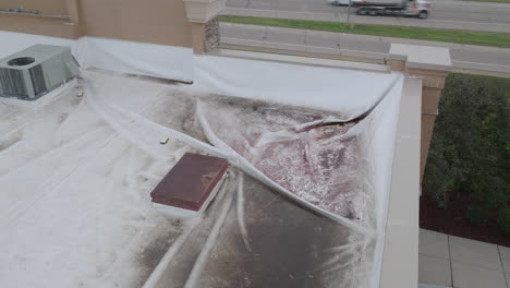 commercial-building-roof-damage-covered-in-white-tarp,-aerial-dynamic