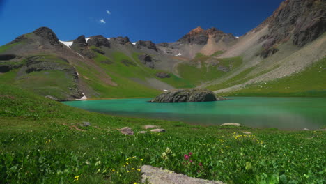 Verträumtes-Colorado-Eis-See-Becken,-Ausgangspunkt,-Oberer-Inselsee,-Unglaubliches-Helles-Aqua,-Blaues-Alpines,-Klares-Wasser,-Sommer,-Blauer-Himmel,-Felsiger-Berg,-Schneegipfel,-Silverton-Tellurid,-Friedliche-Blumen,-Schwenkbewegung-Nach-Links