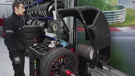 Tire-workshop-technician-in-uniform-using-auto-wheel-balancer-machine-to-repair-wheel