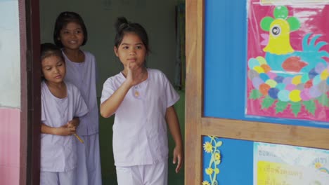 In-a-Thai-classroom,-three-cheerful-girls-warmly-greet-with-waves,-radiating-happiness-and-positivity