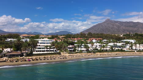 Aerial-view-of-Marbella-beach-and-apartments-with-a-mountain-view,-luxury-vacation-homes-in-Spain,-Malaga-holiday-destination,-4K-shot-moving-forwards