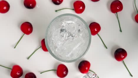 Static-birdseye-shot-of-clear-ice-cubes-falling-into-the-glass-for-a-cool-drink-while-cherries-lie-on-the-side-in-slow-motion