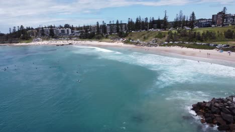 Drone-flying-towards-a-beach-showing-surfers-below-and-a-coastal-town-in-the-background