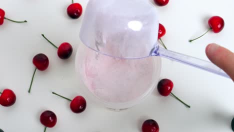Static-Birdseye-shot-from-a-shaker-and-spoon-with-tasty-cherry-Whey-powder-which-is-added-with-surrounding-cherries-on-white-base