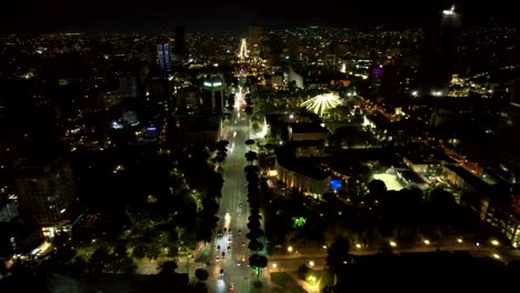 Tirana-capital-of-Albania,-main-boulevard,-institutional-and-historic-buildings-illuminated-at-night,-aerial-drone-shot
