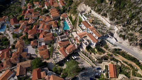 Cinematic-aerial-drone-landscape-of-touristic-village-of-Dhermi-in-Albania,-red-roof-stone-houses-and-cobblestones-on-hills-above-beautiful-shoreline-of-Ionian-sea
