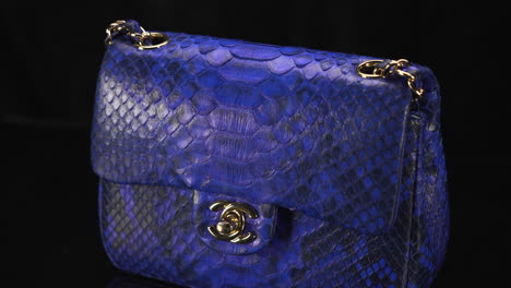Exotic-blue-snakeskin-Chanel-handbag-turning-with-black-background,-expensive-luxury-product-made-of-real-leather,-4K-shot