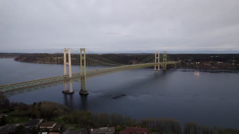 The-Tacoma-narrows-bridge-spanning-the-Calm-waters-of-Puget-Sound,-wide-aerial-orbit