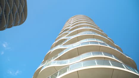 tall-modern-buildings-all-white-glass-balcony-wavy-futuristic-looking-unusual-design-luxury-architecture-holiday-resort-bottom-looking-up-view-moving-wide-shot-sign-post-over-the-frame-clear-blue-sky