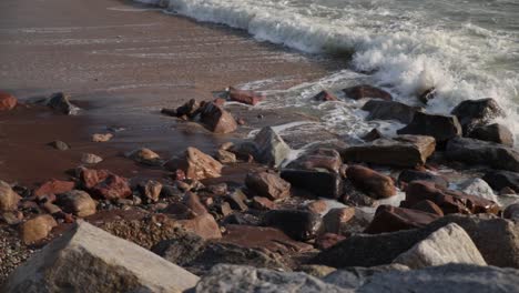 Waves-crashing-on-multicolored-rocks-and-red-sand-on-a-beach-in-Swakopmund,-Namibia