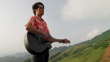 Hombre-Asiático-Tocando-Guitarra-Acústica-Al-Aire-Libre-En-La-Naturaleza,-Plano-Medio