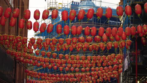 Viele-Rote-Laternen-Hängen-In-China-Town-Mitten-Auf-Der-Straße-über-Windigem-Wetter-Und-Fliegen-Um-Die-Baustelle-Herum,-Im-Hintergrund-Ist-Blaues-Material-Um-Das-Reparierende-Gebäude-Gewickelt