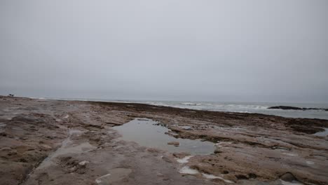 A-puddle-on-a-rocky-beach-with-the-ocean-in-the-background-on-a-cloudy-day