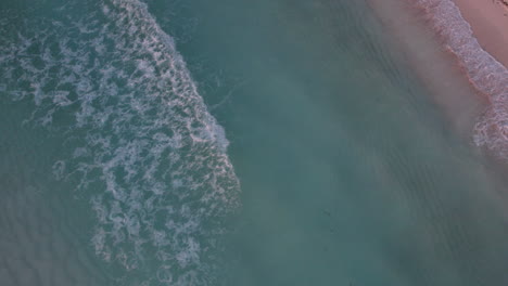 Aerial-Top-down-shot-of-rolling-waves-in-a-crystal-clear-blue-ocean-with-white-sand-beach-in-Cancun,-Mexico