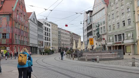 People-Walking-In-Maximilianstrasse-Street-With-Tramway-Tracks,-Weberhaus-Augsburg-And-Merkur-Brunnen-Fountain-In-Germany