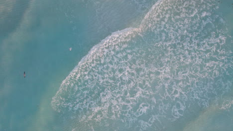 Aerial-Top-down-shot-of-rolling-waves-in-a-crystal-clear-blue-ocean-with-white-sand-beach-as-birds-fly-gracefully-above-the-water-in-Cancun,-Mexico