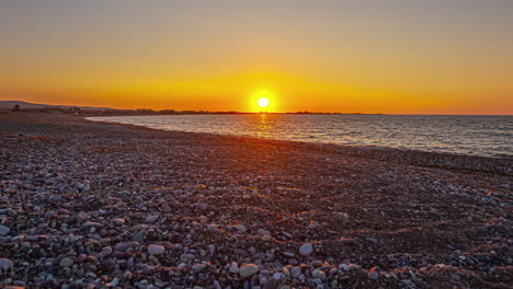 Sunrise-over-Pebble-Beach,-Calming,-Golden-Yellow-Sun,-Still-Ocean,-Peaceful-Zen-Timelapse,-Static,-Wide-Angle