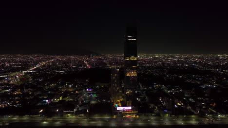 Drone-shot-circling-in-front-of-the-illuminated-Torres-Obispado-skyscraper-complex,-night-in-Monterrey,-Mexico