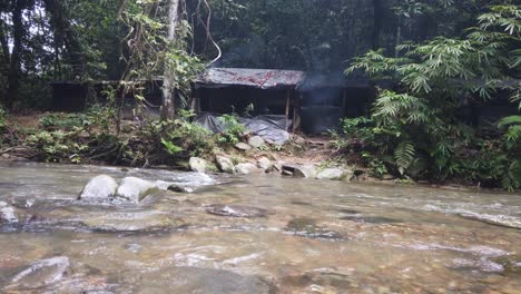 Tilting-shot-of-a-campsite-in-a-rainforest-with-a-small-river-in-front