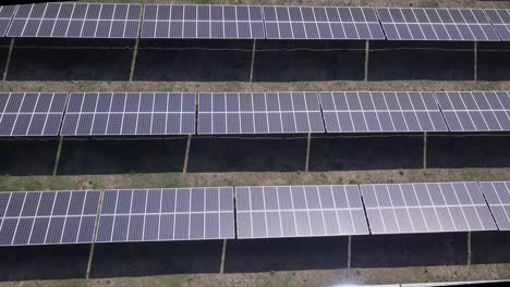 Sun-reflects-off-array-of-black-solar-panels-in-low-aerial-flyover