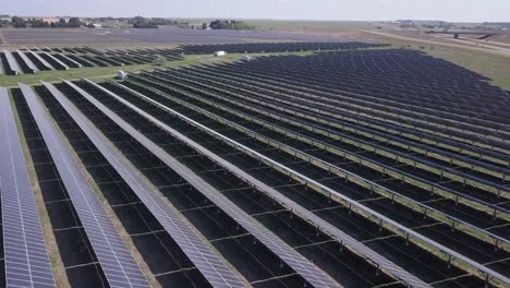 Huge-solar-panel-array-in-prairie-field-beside-rural-highway,-aerial