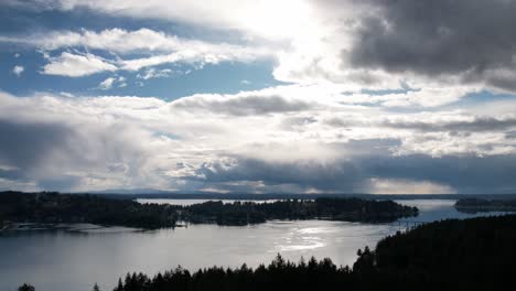 Dramatic-rolling-clouds-reflect-afternoon-sunshine-on-pristine,-Puget-sound,-Washington,-aerial-hyper-lapse