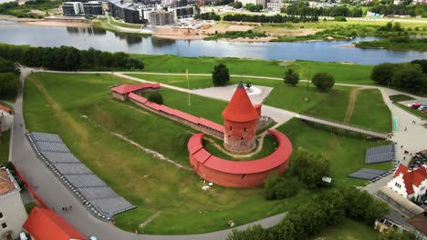 Drone-shot-of-the-historic-old-red-brick-Kaunas-Castle-with-Vytis-statue-and-Ukrainian-flag-near-the-Nemunas-river-in-Kaunas-old-town,-Lithuania-on-a-sunny-day,-parallax-shot