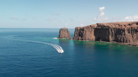 Roque-Partido,-Gran-Canaria:-aerial-view-of-an-approaching-boat-with-Roque-Partido-in-the-background-on-a-sunny-day