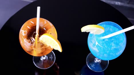 Slow-orbiting-shot-showing-a-blue-and-an-orange-freshly-made-cocktail-with-garnish