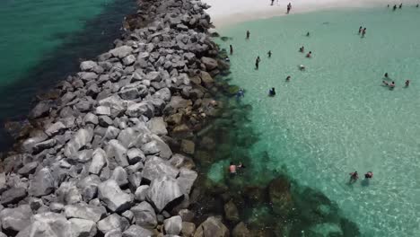 Aerial-view-of-People-tourist-snorkeling-swimming-in-the-Green-crystal-clear-waters,-Blue-skies,-and-white-sands,-at-Shell-island-on-Florida’s-Emerald-Coast